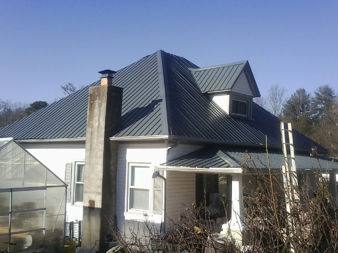Dark blue standing seam metal roof on a white farmhouse with dormer — Slate & Tile Roof Repair by Roofing Brothers in Cedar Mountain