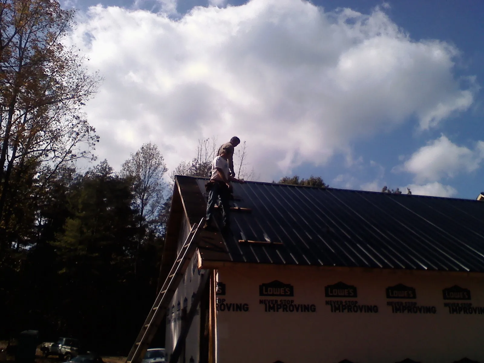 Roofer fastening dark metal panels high against a cloudy sky, from a Roof Inspection job in Cedar Mountain