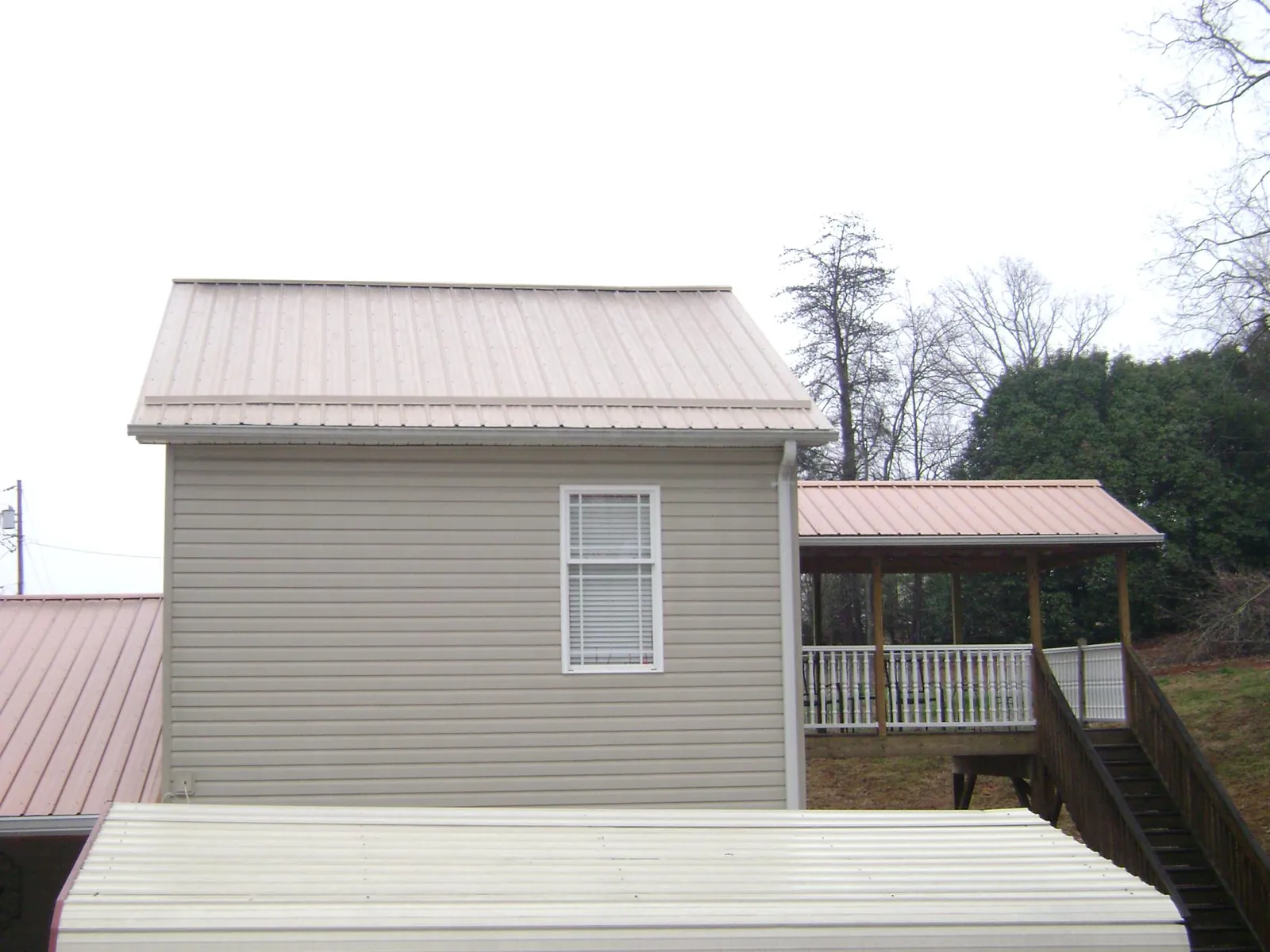 Tan metal roofs on a two story addition and attached porch, from a Roof Replacement job in Cedar Mountain